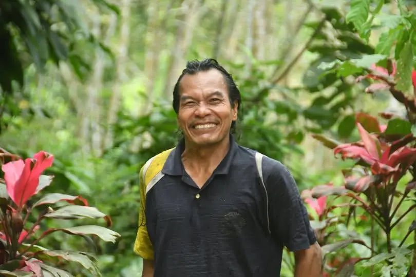 Portrait of Jos, smiling broadly, standing waist-up in the middle of the green jungle